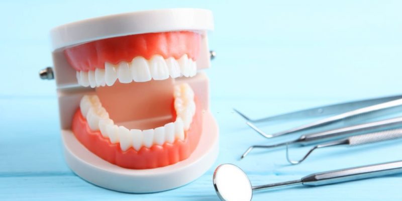 model of teeth and dental instruments and dental care products on colored background
